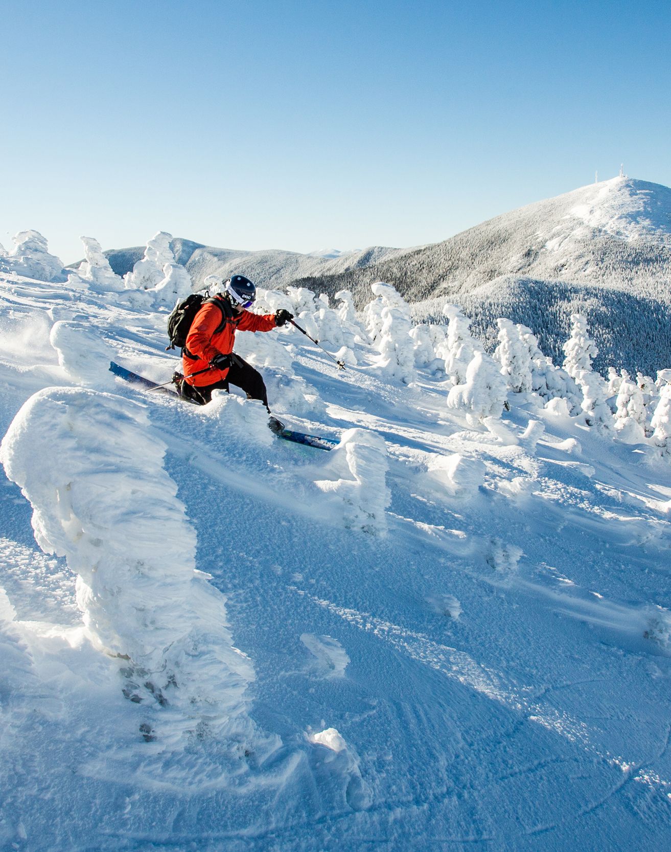 Tele skier on summit of Burnt Mountain on a snowy morning with Sugarloaf in view behind
