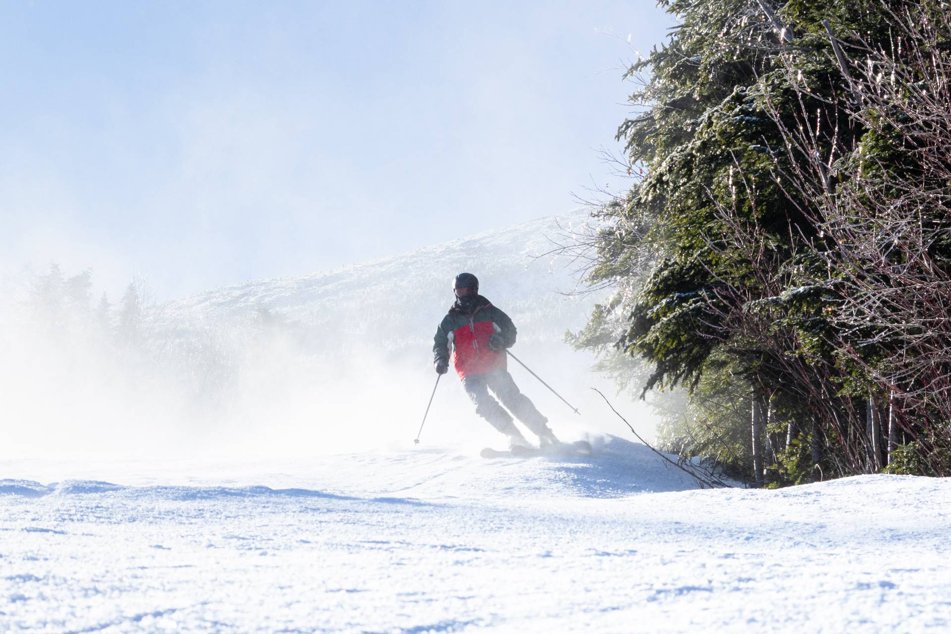 A skier turns down a slope with a mountain behind him.
