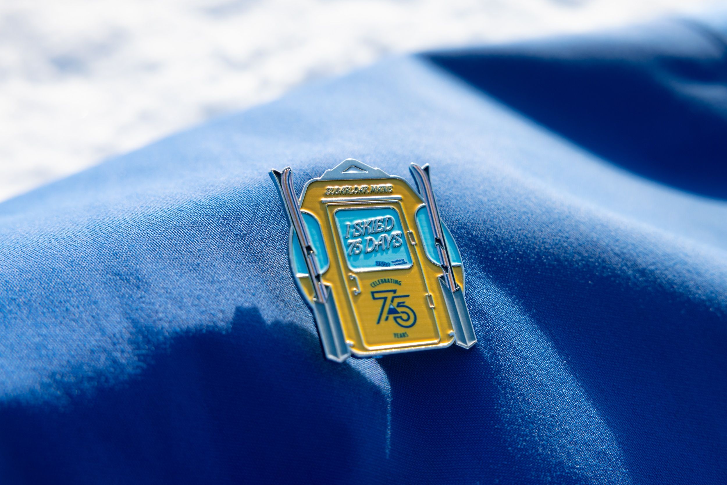75th skier day pin on blue fabric backdrop