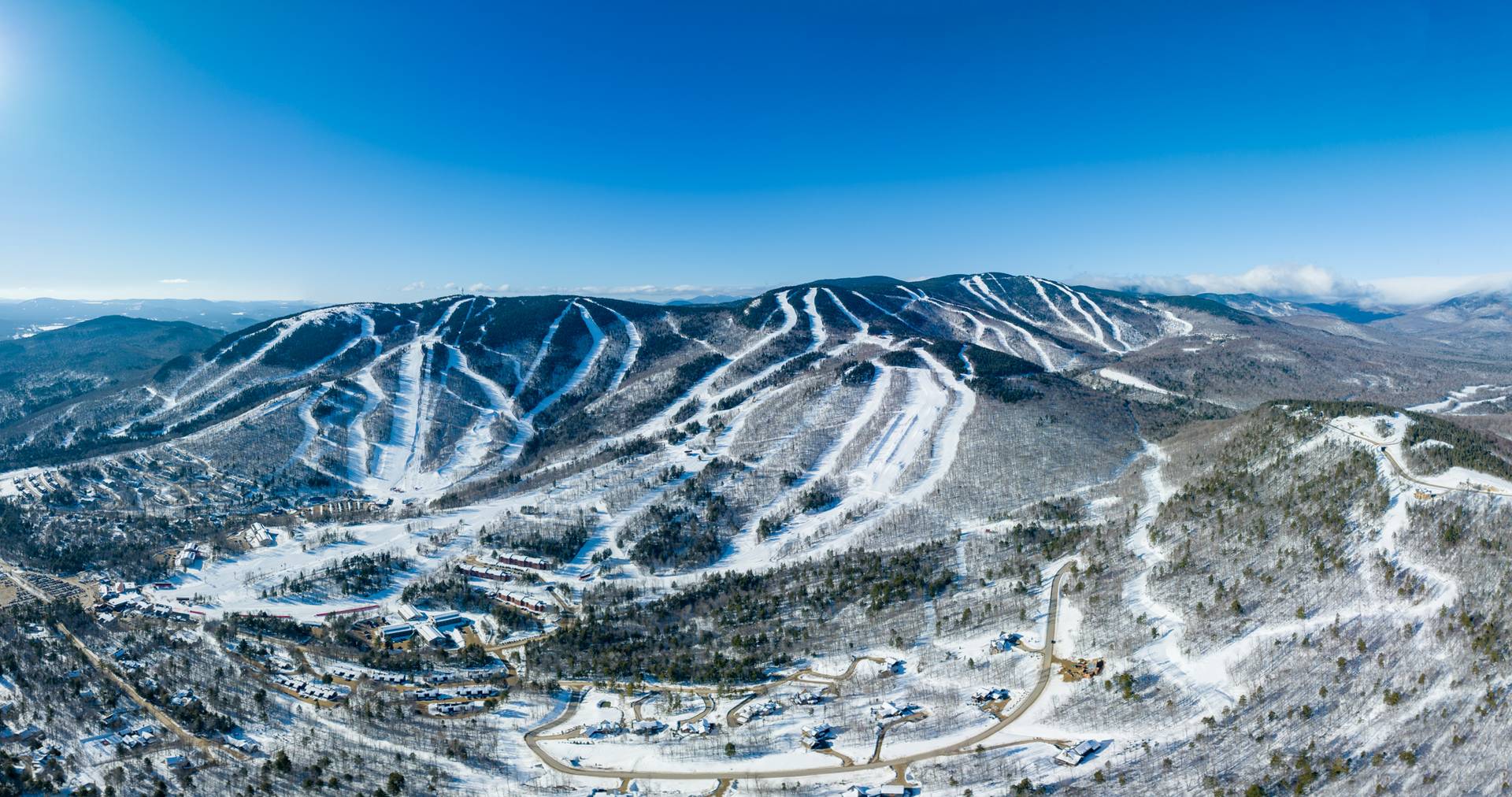 An aerial view of Sunday River Resort in the winter with blue skies and green trees.