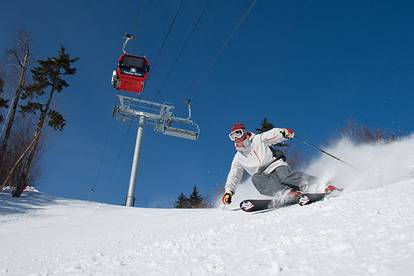A skier shredding down a trail with the Sunday River Chondola in the background.