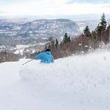 A man skiing down a trail, with snow coming up, at Sunday River.