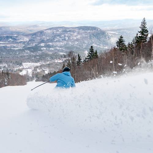 A man skiing down a trail, with snow coming up, at Sunday River.
