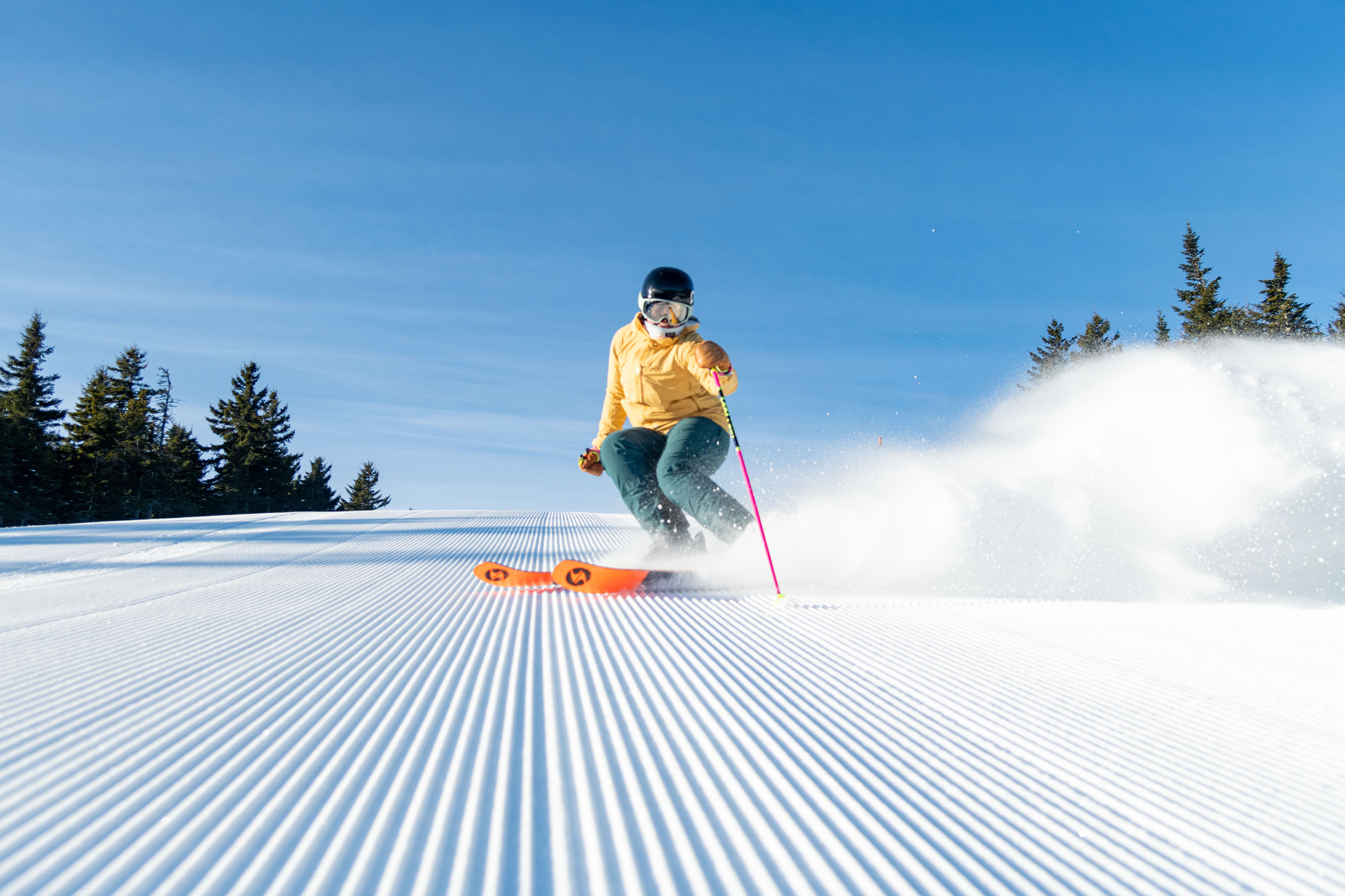 A person in a yellow and green kit skiing down a trail at Sunday River.