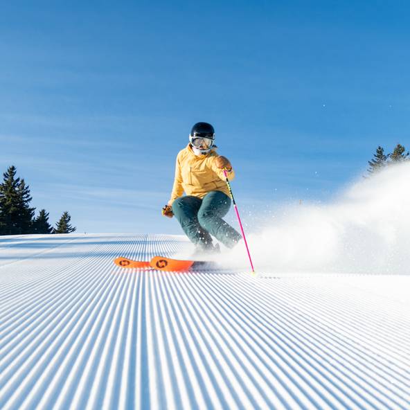 A person in a yellow and green kit skiing down a trail at Sunday River.