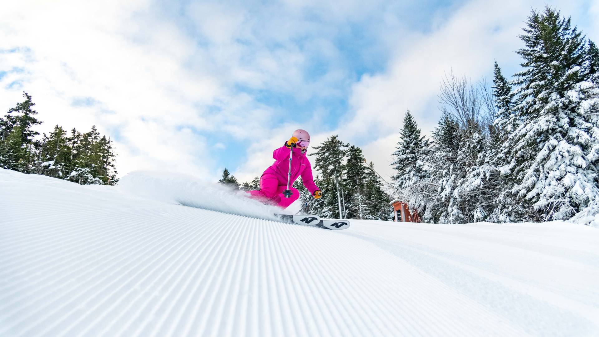 A woman skiing on fresh stripes with blue skies at Sunday River.