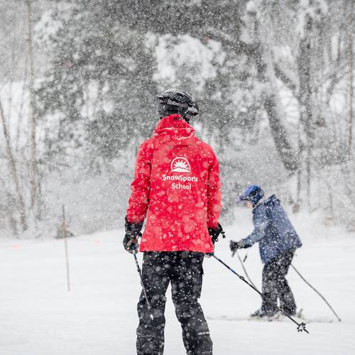 An instructor with the Sunday River SnowSports School giving an adult a lesson while it's snowing.