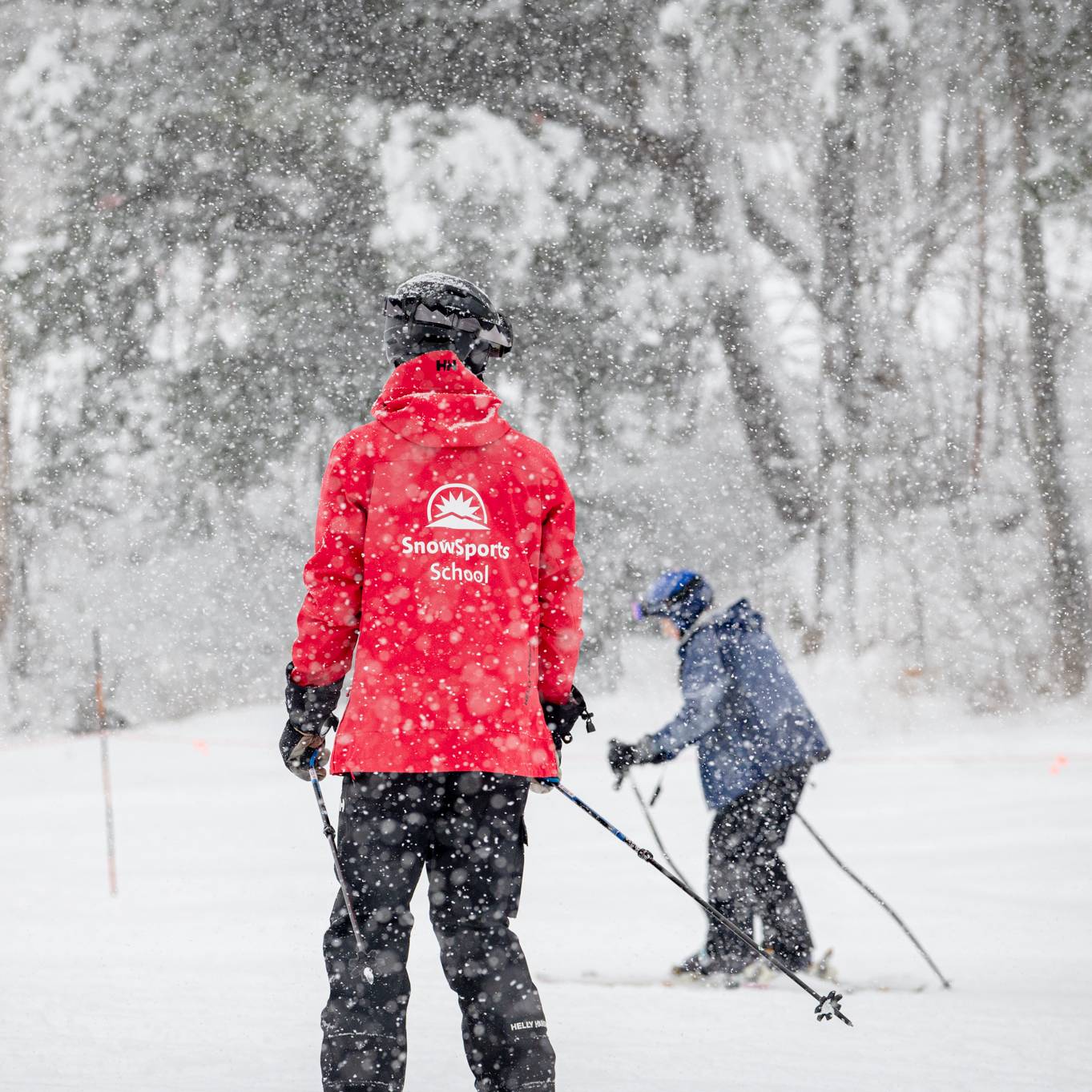 A SnowSports School instructor teaching a skier how to ski at Sunday River while it's snowing.