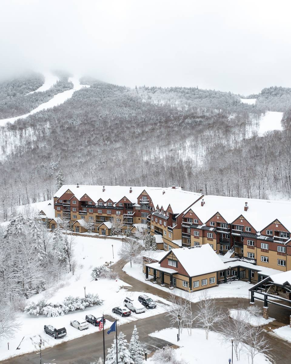 The Jordan Hotel at Sunday River with snow covering the exterior and the mountains.