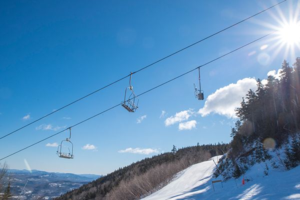 Chairs in the air from the Aurora chairlift at Sunday River, with blue skies in the background and snow on the ground.