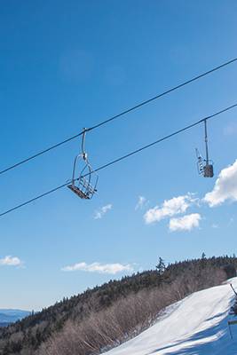 Chairs in the air from the Aurora chairlift at Sunday River, with blue skies in the background and snow on the ground.