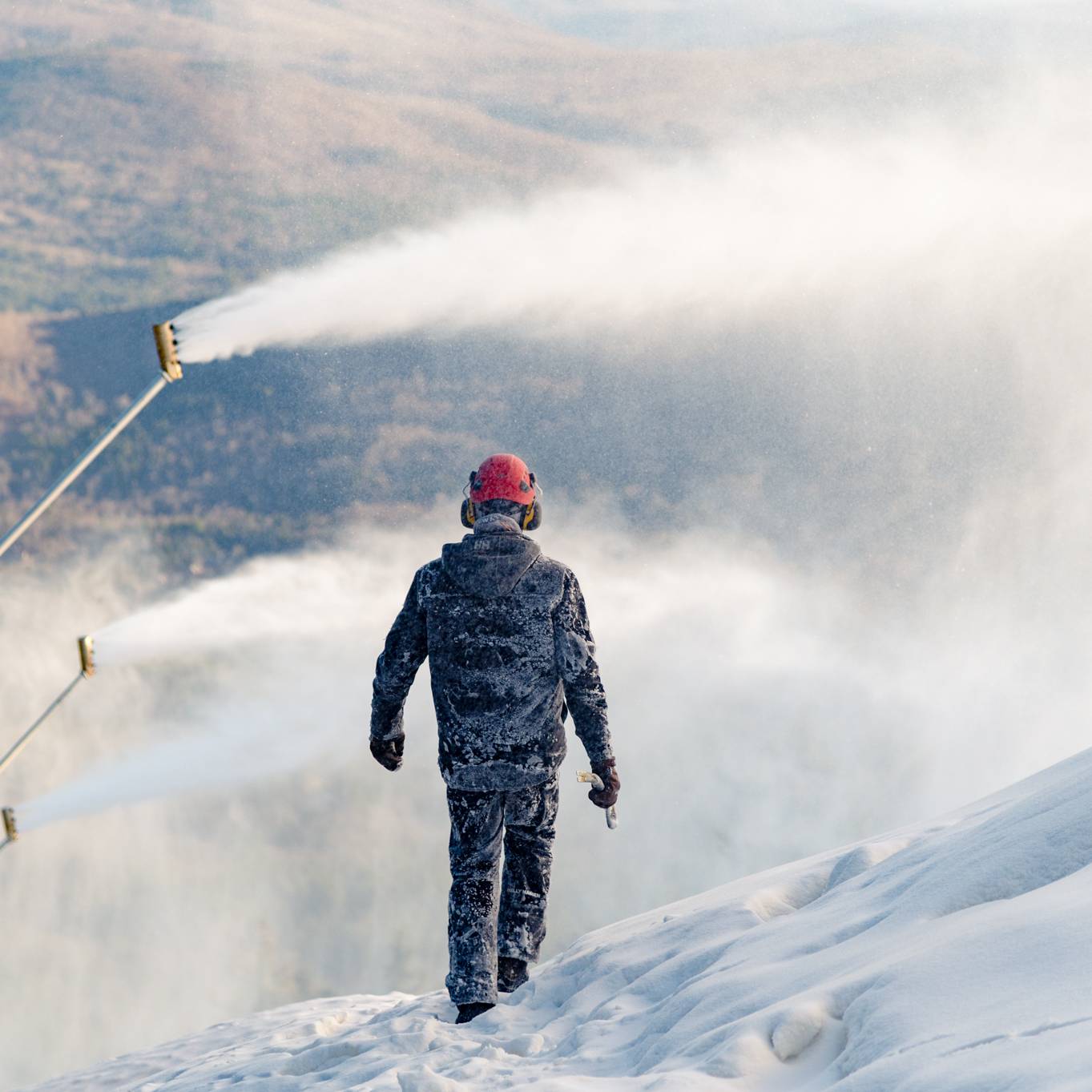 A man walking around piles of snow while they are making snow at Sunday River.