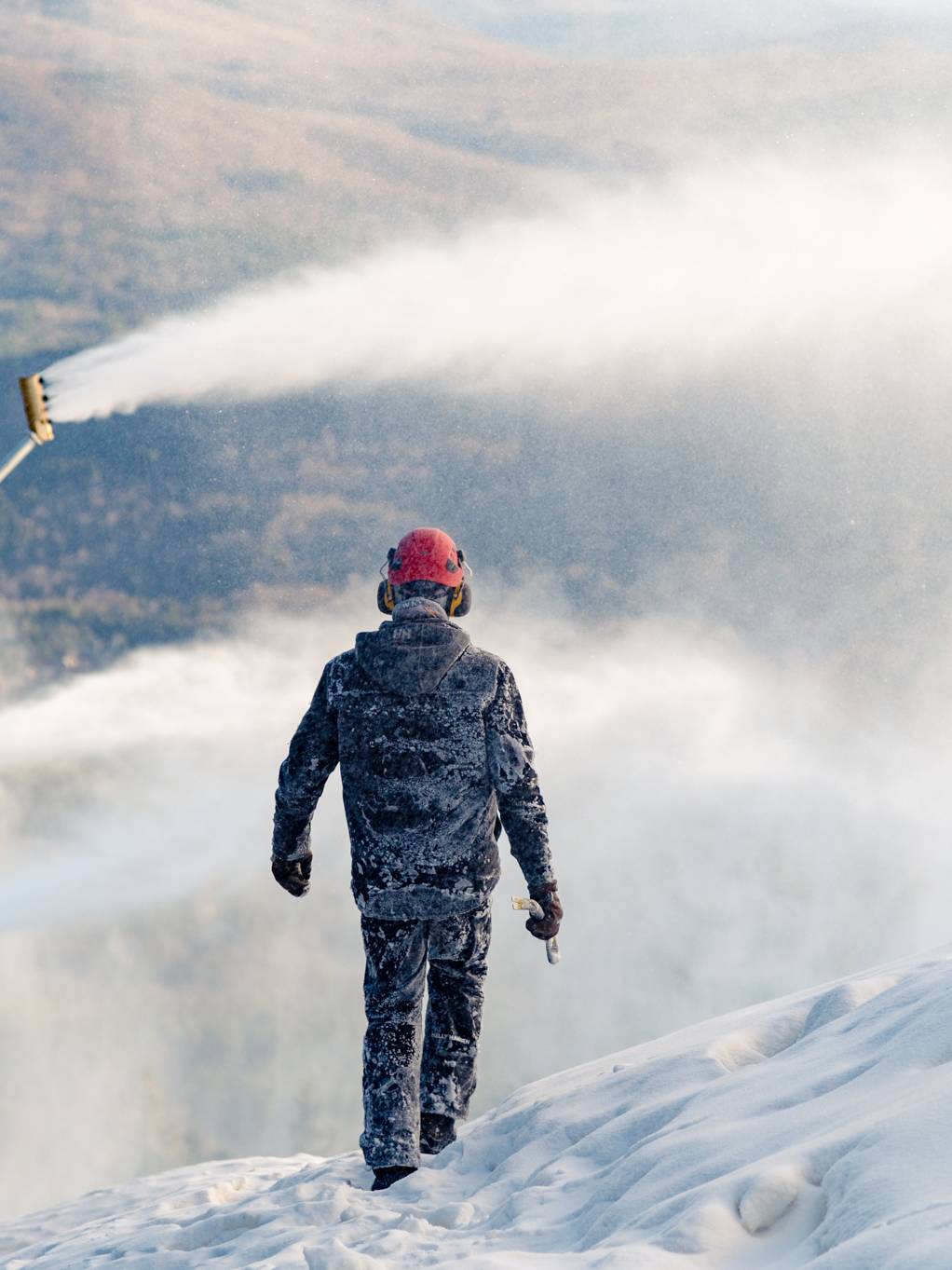 A man walking around piles of snow while they are making snow at Sunday River.