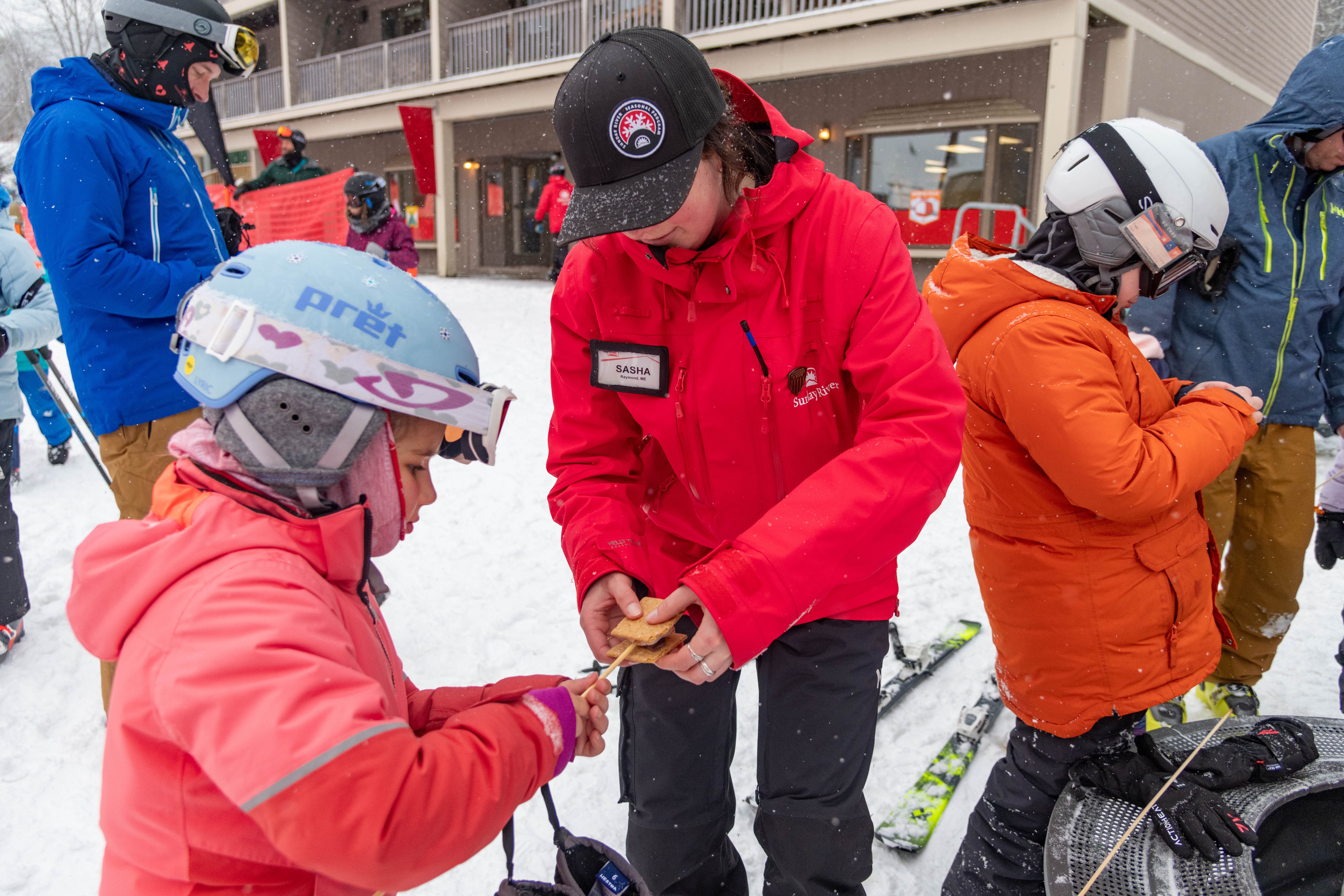 A team member from Sunday River helping a kid make a smore.
