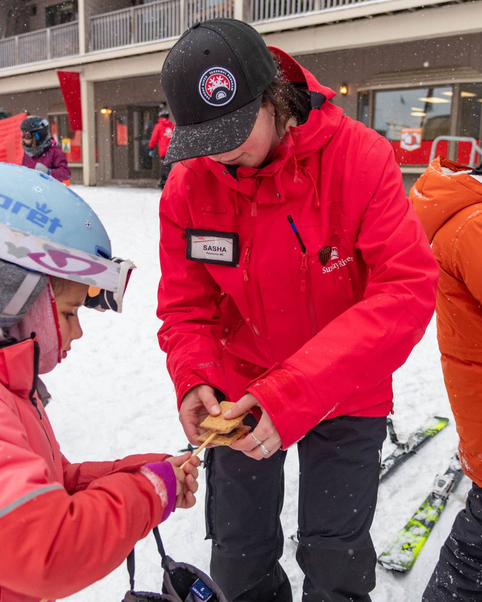 A team member from Sunday River helping a kid make a smore.