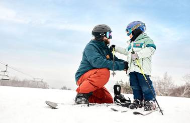 A man helping a child with their skis on snow at Sunday River.