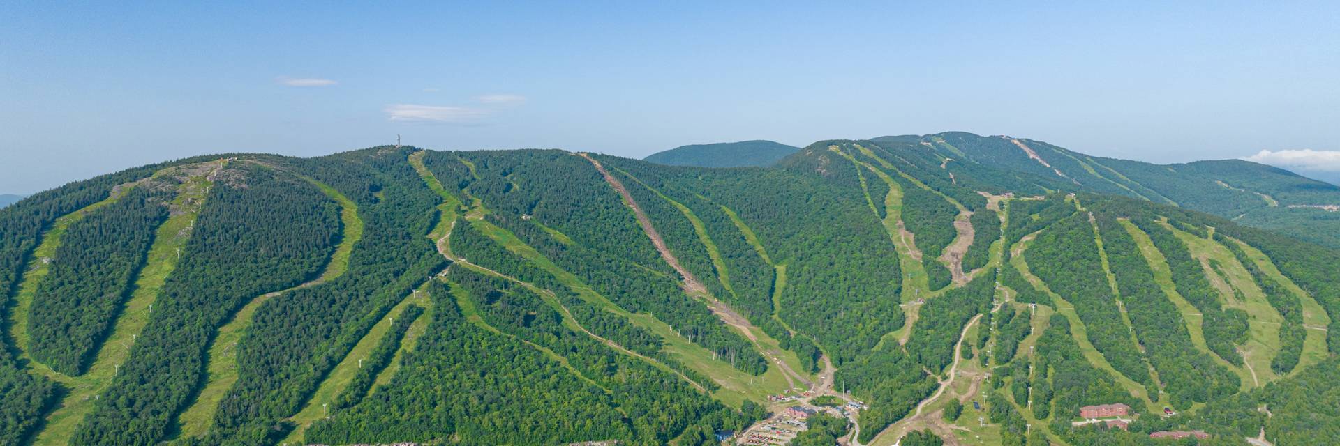 An aerial view of Sunday River Resort in summer with blue skies and green trees.