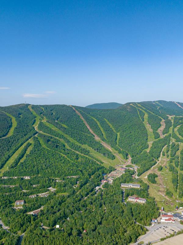 An aerial view of Sunday River Resort in summer with blue skies and green trees.