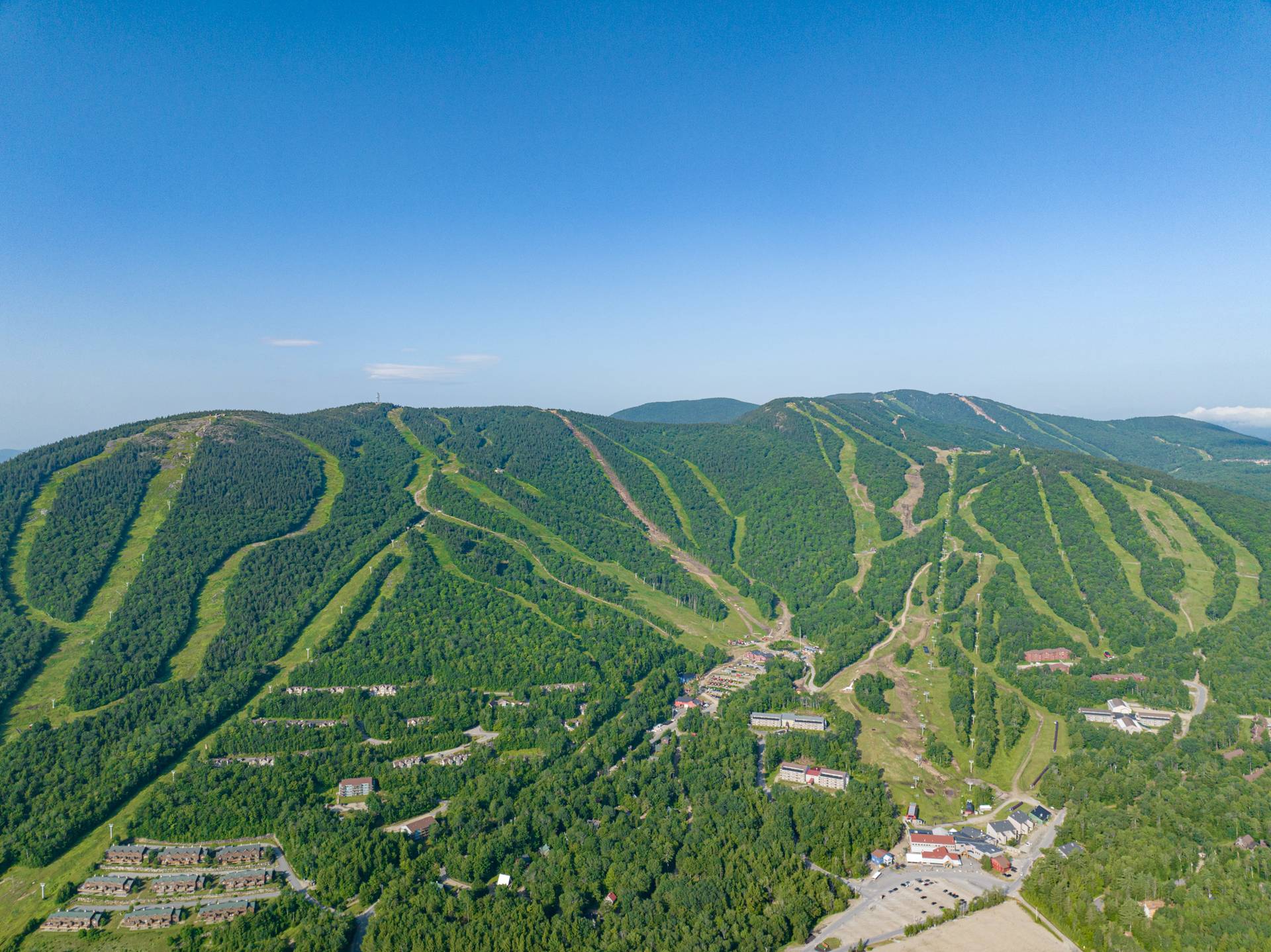 An aerial view of Sunday River Resort in the summer with blue skies and green trees.