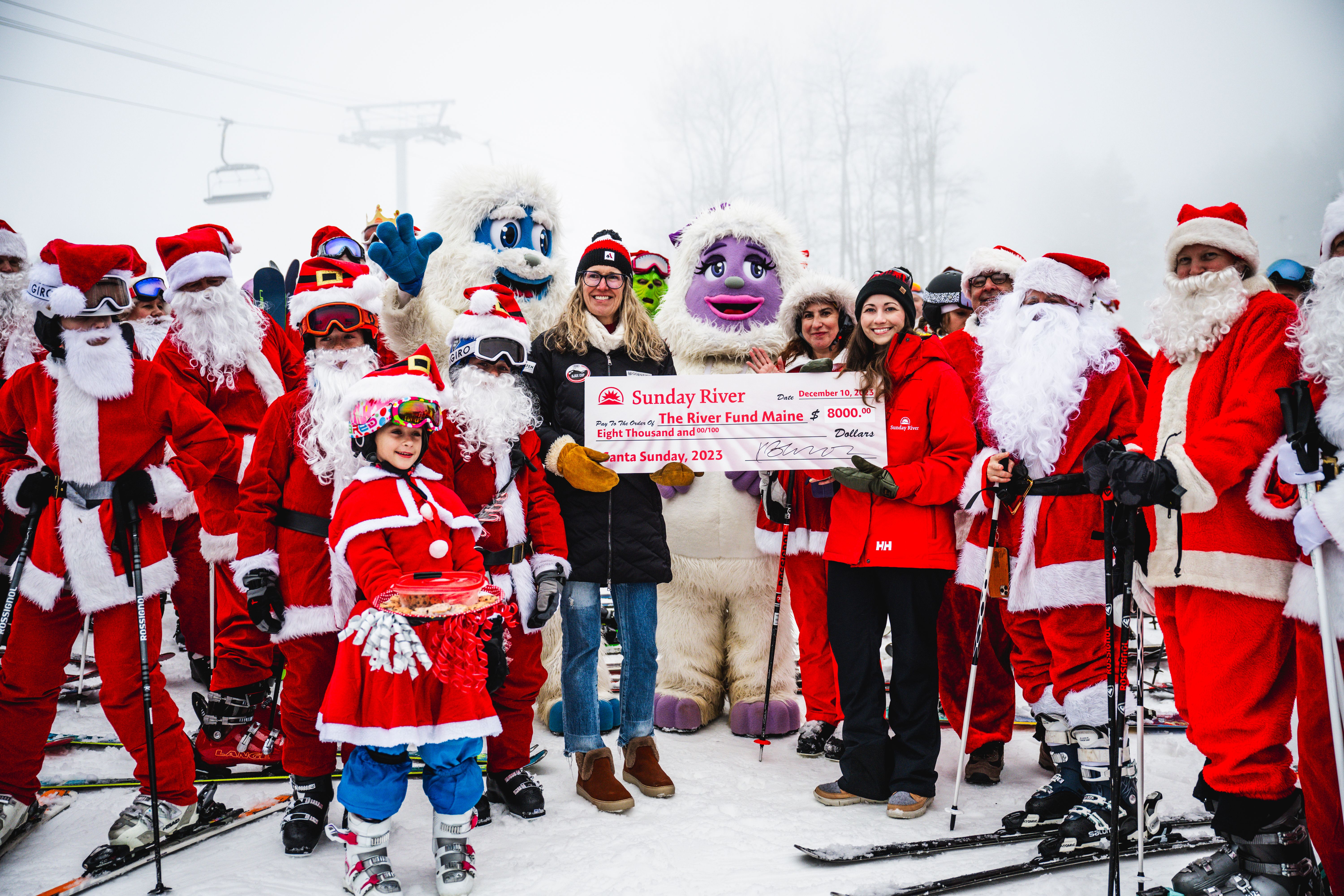Skiers dressed as Santa during Sunday River's Santa Sunday, presenting a check to The River Fund Maine.