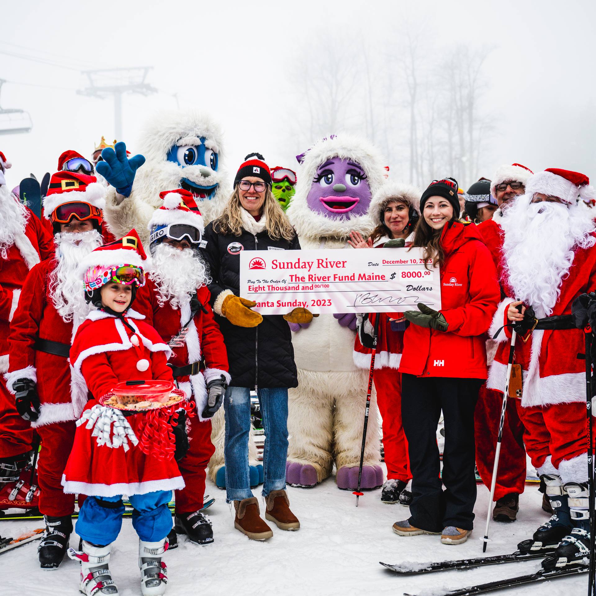 Skiers dressed as Santa, with a check being presented to The River Fund Maine, at Sunday River's Santa Sunday.