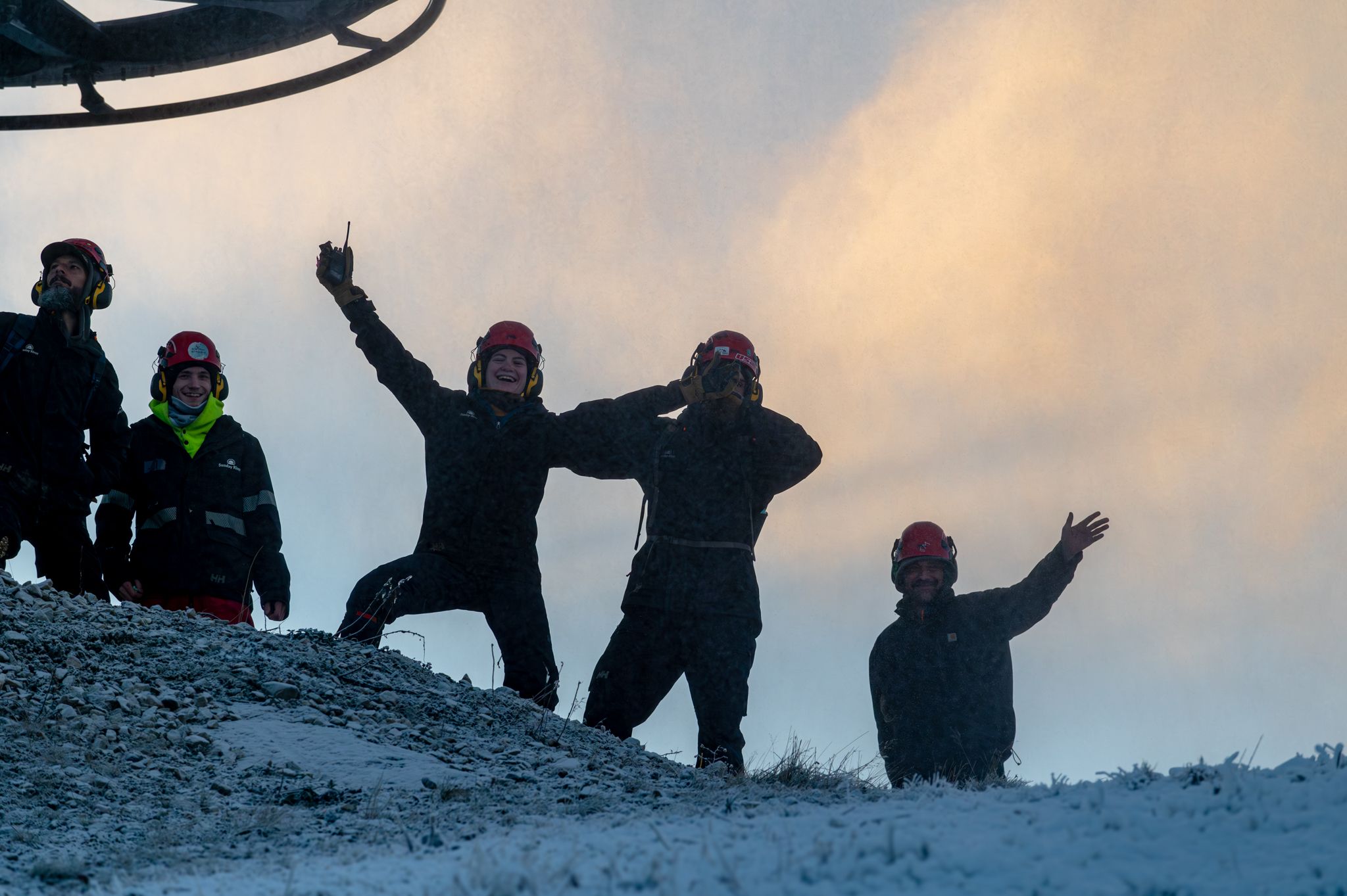 Snowmakers smiling and posing for the camera at Sunday River, with snowmaking going on in the background.