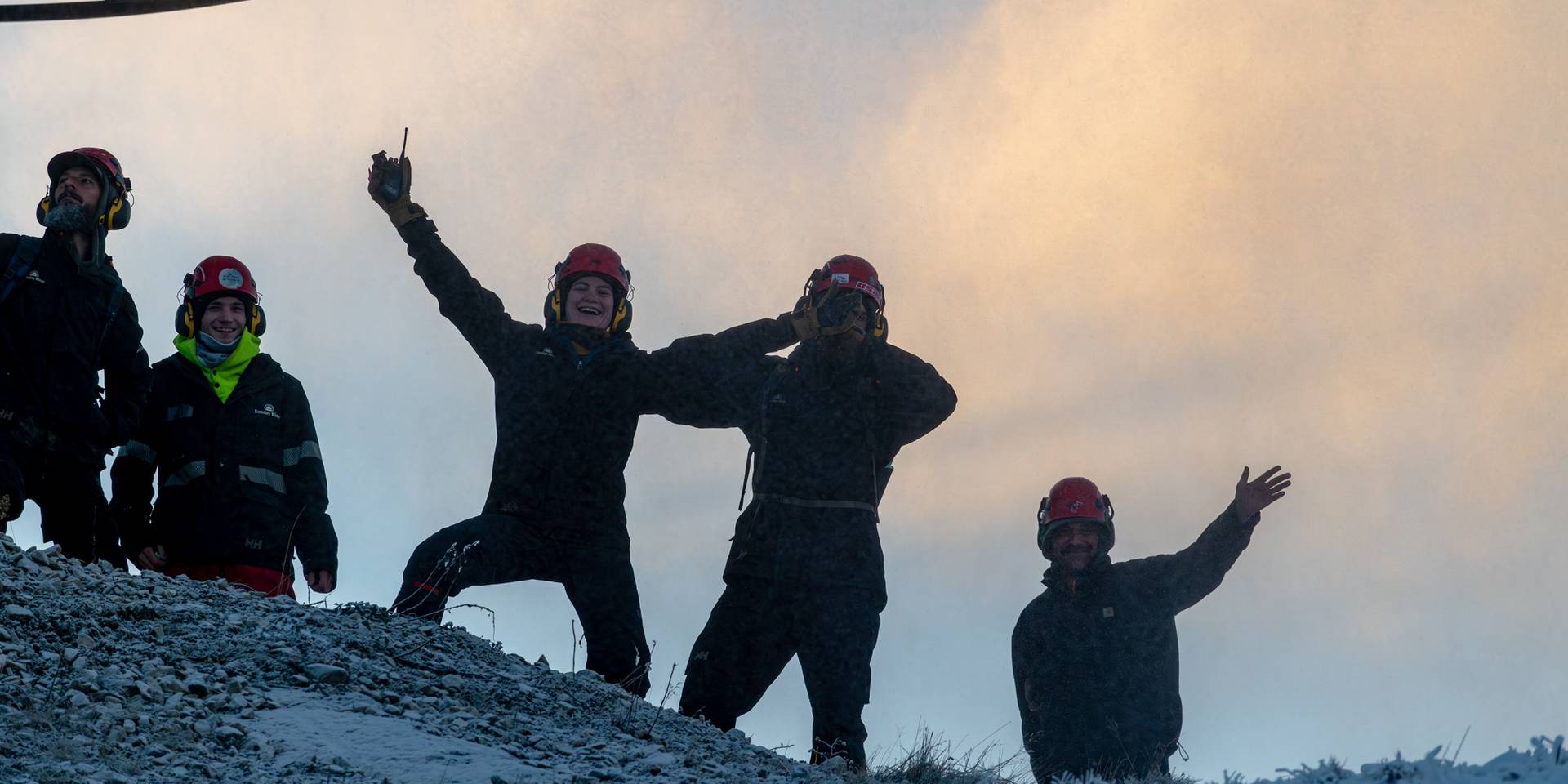 Snowmakers smiling and posing for the camera at Sunday River, with snowmaking going on in the background.