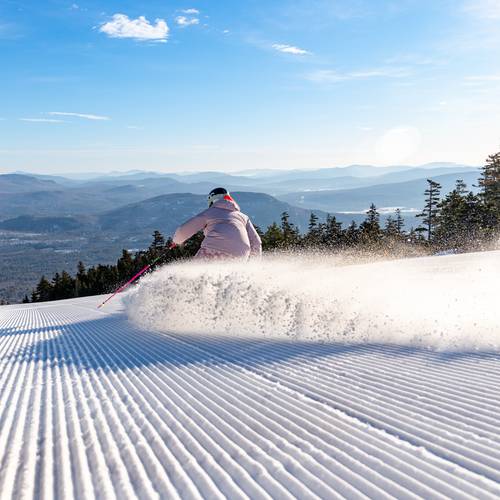 A woman skiing down a trail at Sunday River under the morning blue sky.