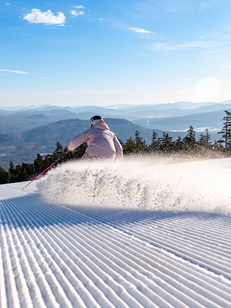 A woman skiing on fresh stripes with blue skies at Sunday River.
