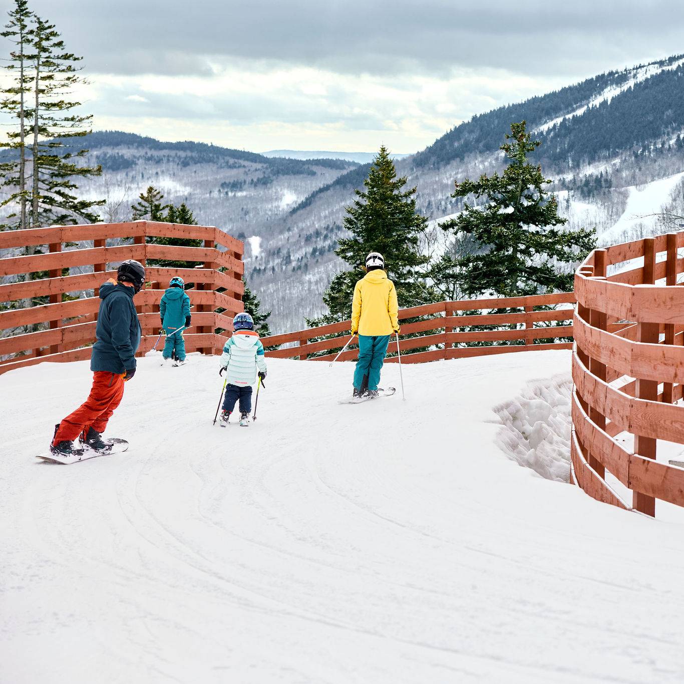 A family skiing across a bridge at Sunday River Resort.