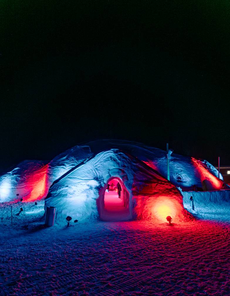 The outside of the Iglu at night with colored lights reflecting on the outside.