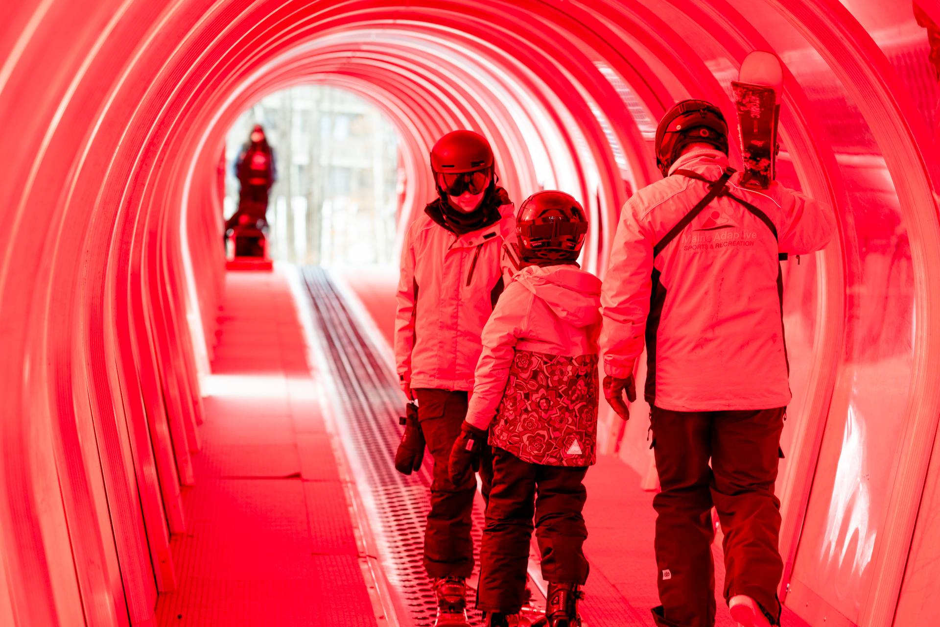 A little girl and her instructors standing in a covered conveyor at Sunday River for a ski lesson.