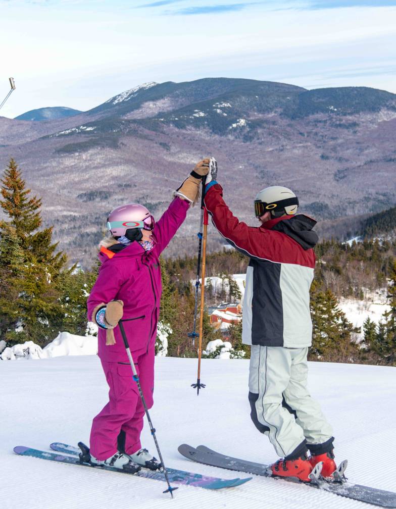 Two skiers high fiving on the top of a Sunday River run.