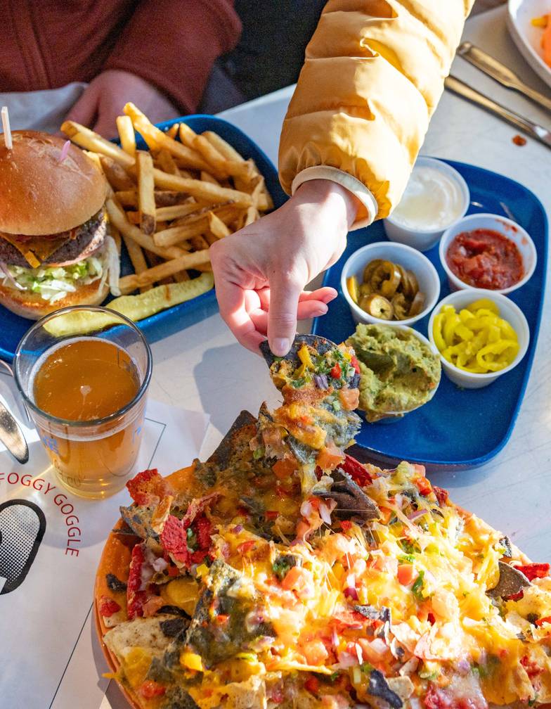 An aerial view of a table of food with people eating at the Foggy Goggle