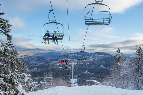 People sitting on a chairlift in the winter, at Sunday River, with blue skies.