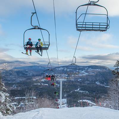 People sitting on a chairlift in the winter, at Sunday River, with blue skies.