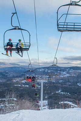 People sitting on a chairlift in the winter, at Sunday River, with blue skies.