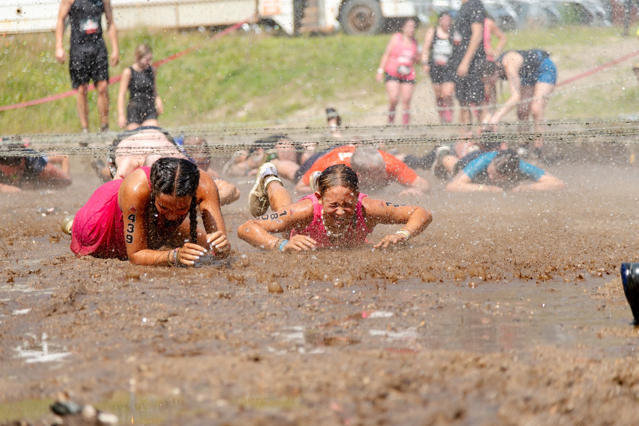 Two girls crawling through mud at Tough Mountain Challenge.