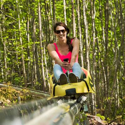 A woman riding on a mountain coaster in the summer time.