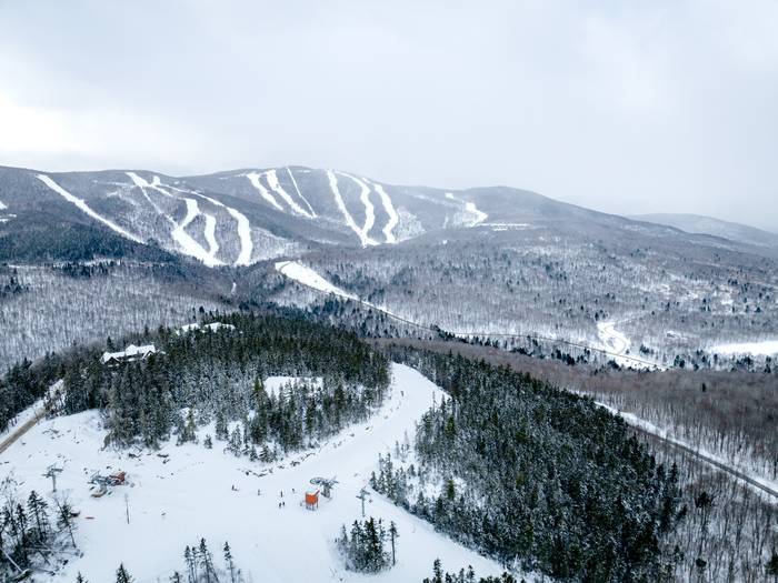 An aerial view of Sunday River's Merrill Hill Triple in the winter, with mountains and trails in the background.
