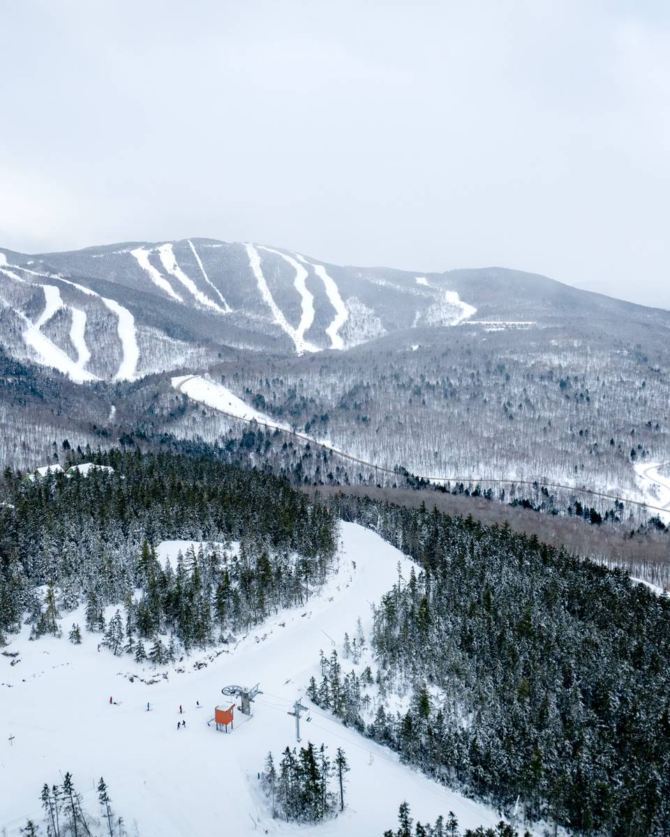 An aerial view of Sunday River's Merrill Hill Triple in the winter, with mountains and trails in the background.