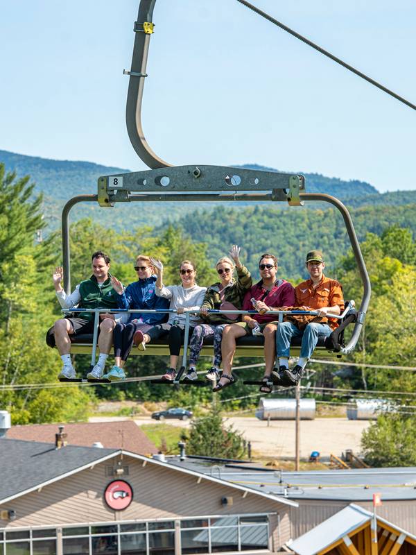 A group of people sitting in a chair on the Chondola for scenic lift rides at Sunday River.