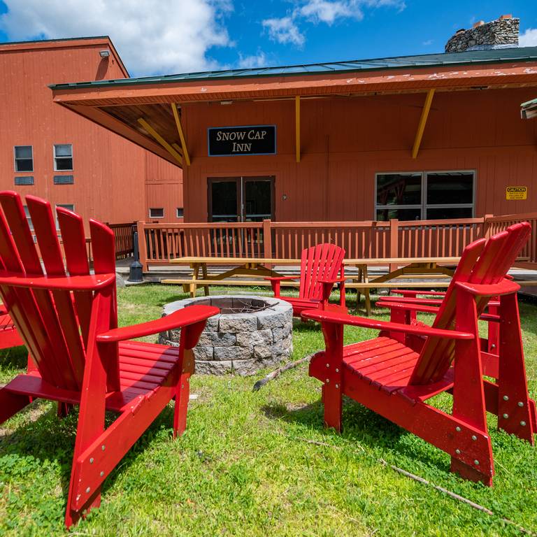 Exterior view of the Snow Cap Inn with chairs around an outdoor firepit - at Sunday River Resort.