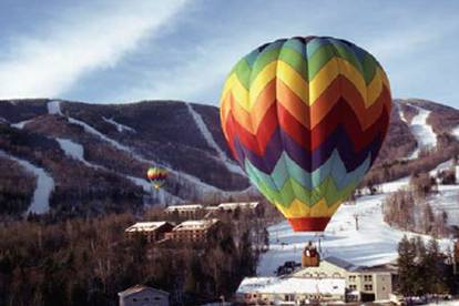 A rainbow chevron hot air balloon flying over the South Ridge lodge at Sunday River.