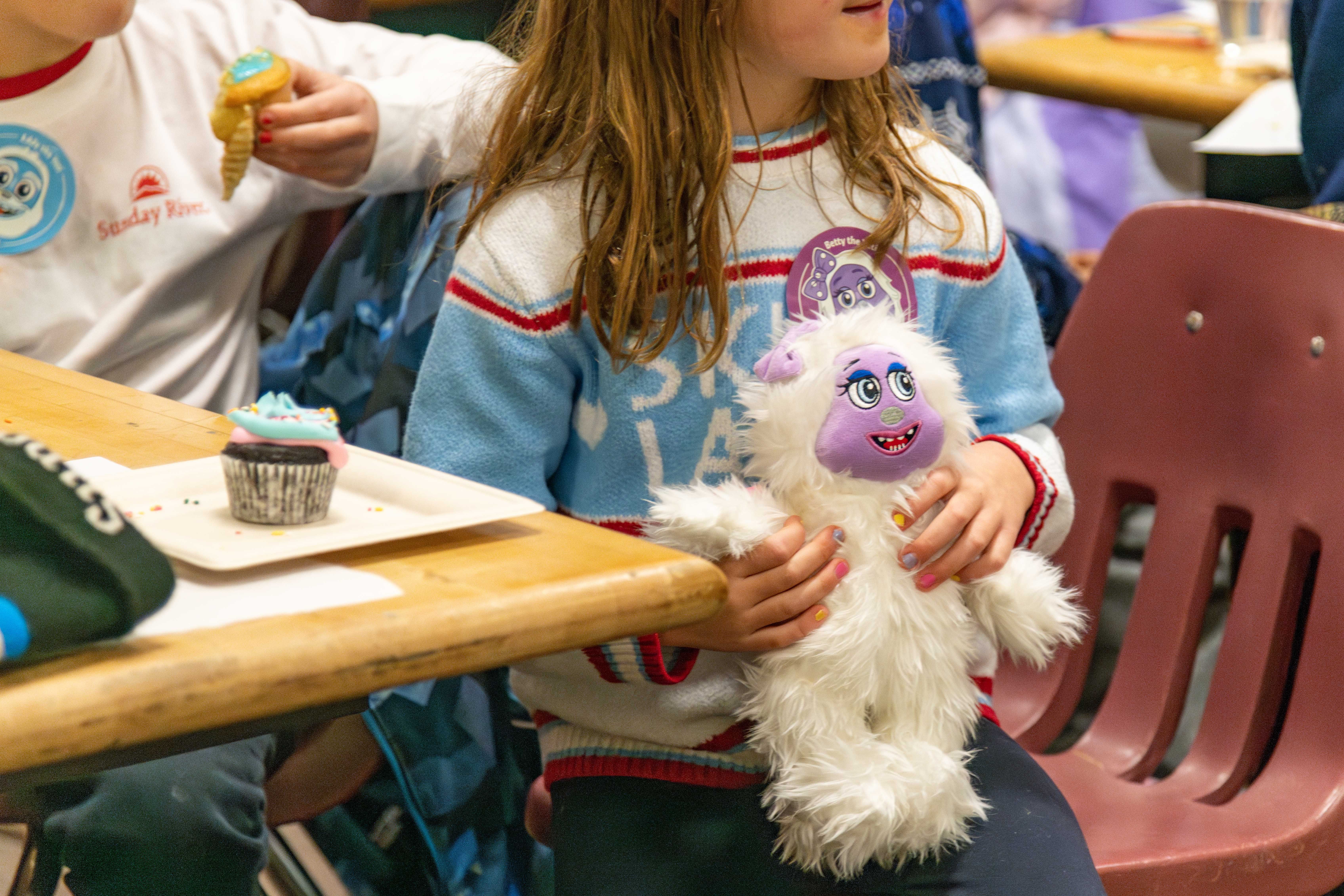 A little girl with her cupcake holding a Betty the Yeti plushy at Sunday River.