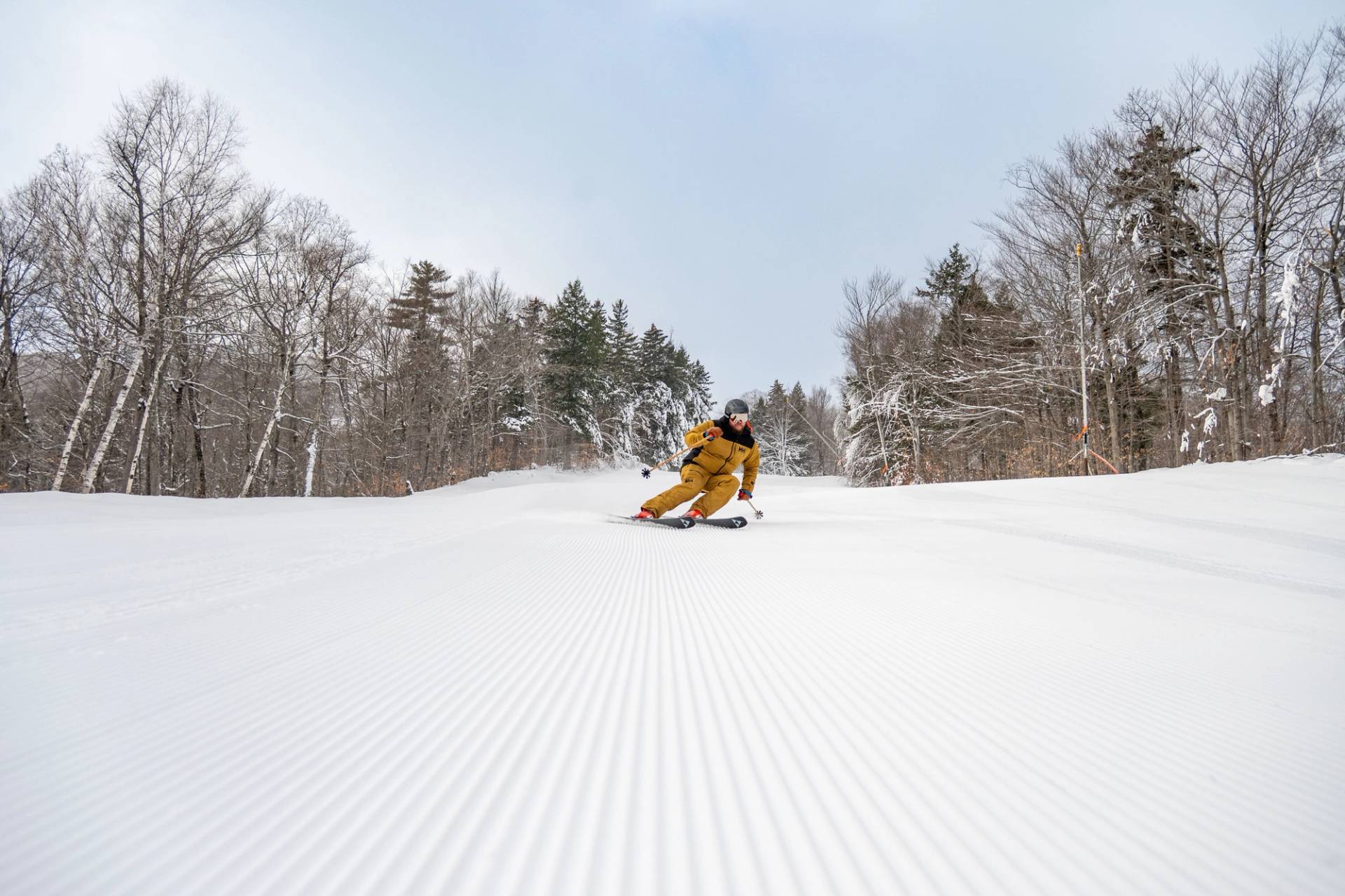 A man in a brown ski outfit skiing on fresh stripes.