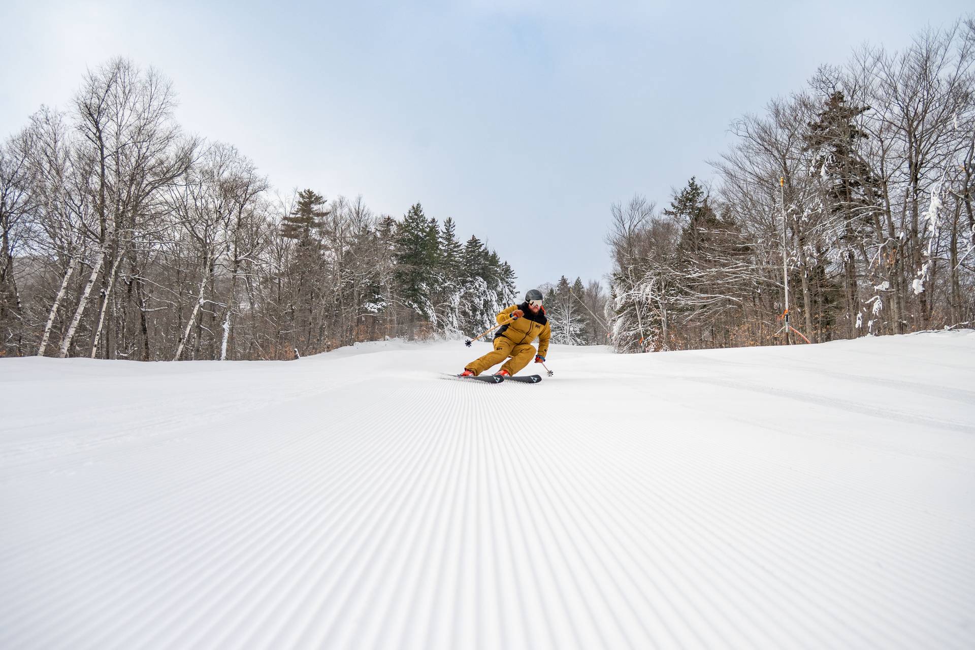 A man in a brown ski outfit skiing on fresh stripes.