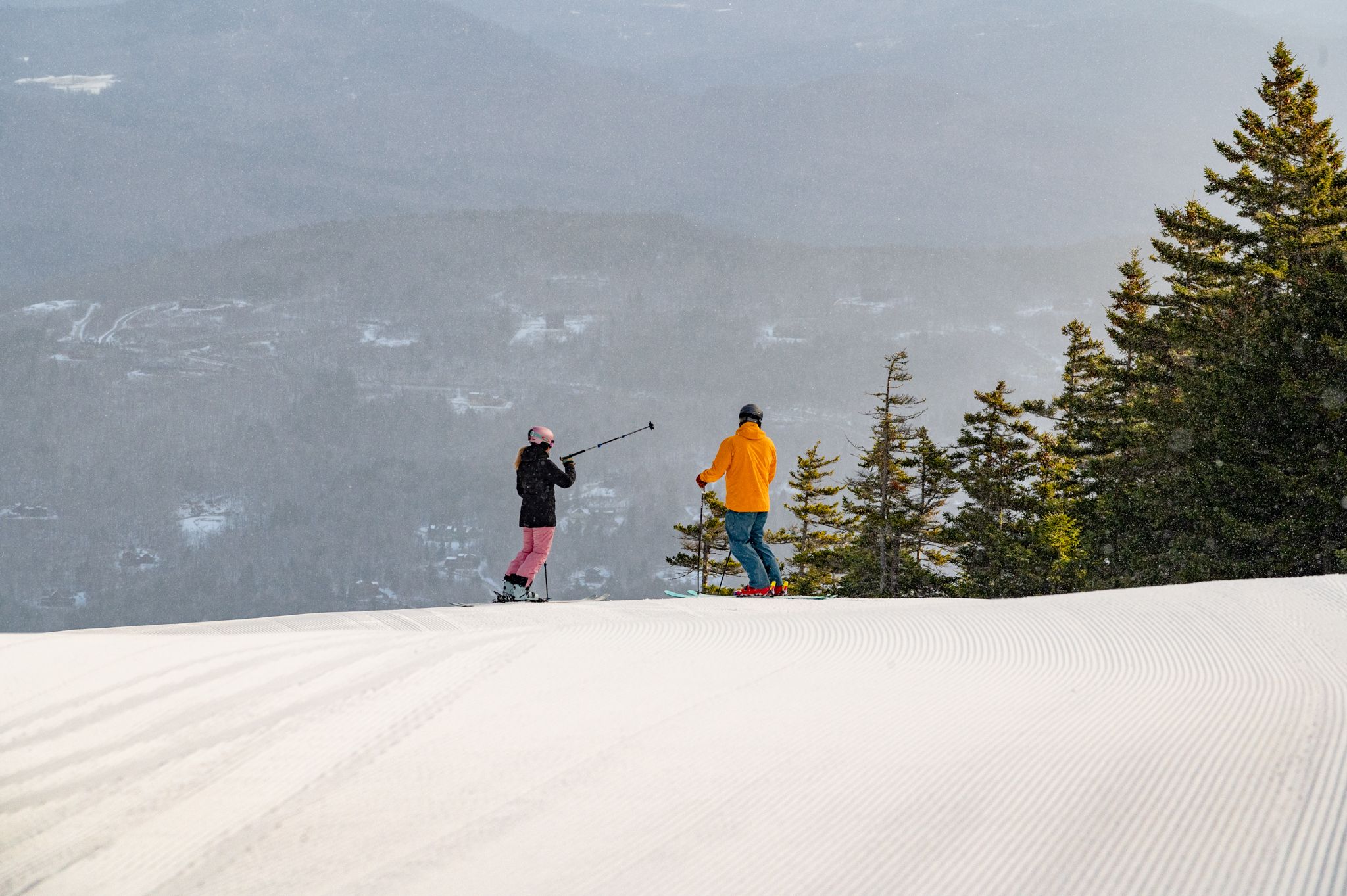 Two skiers at the top of a ski trail, pointing over to the woods, on a sunny day at Sunday River Resort.