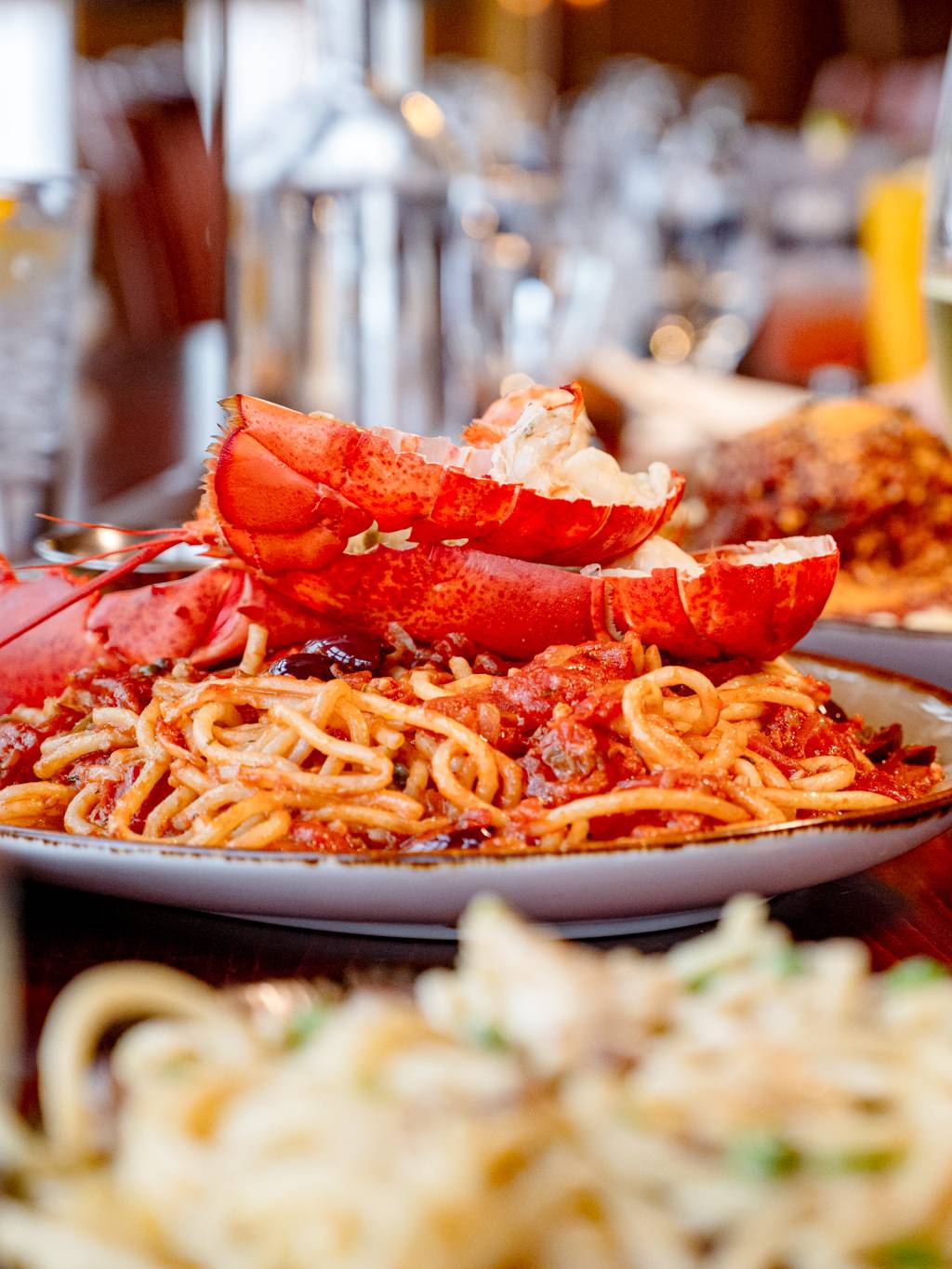 Lobster pasta and a glass of wine in the foreground with several other dishes on the table.