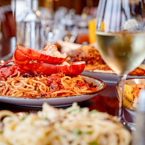 A pasta and lobster dish with a glass of wine.